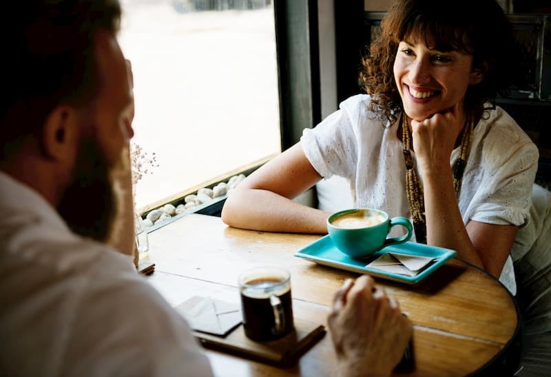 Middle aged brunette woman and man with a bear chatting over a cup of coffee | The Mental Health Survival Guide to Post-Grad Life | e-Surgery