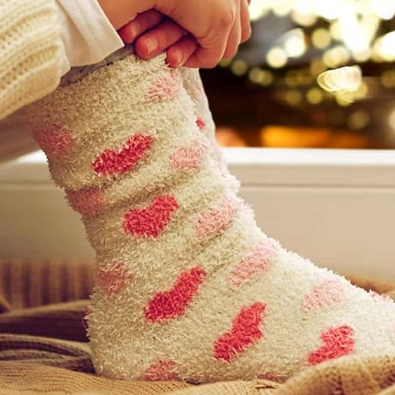 Young woman with knees up to chest looking out at Christmas scene, loneliness at Christmas, e-Surgery