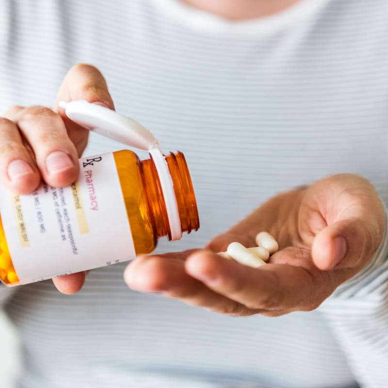 person pouring a pot of pills into their hand statin side effects | e-Surgery