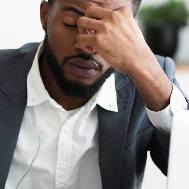 Anaemia, middle aged black male business man sitting at a laptop looking tired | e-Surgery