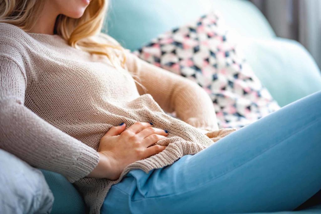 Young blonde woman on a sofa with dark blue painted nails holding her stomach | Trust Your Gut: Can Healthy Bacteria Make You Happy? | e-Surgery