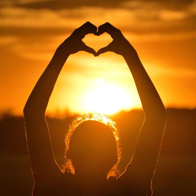 Person holding heart shape with their hands in the sky at sunset | e-Surgery