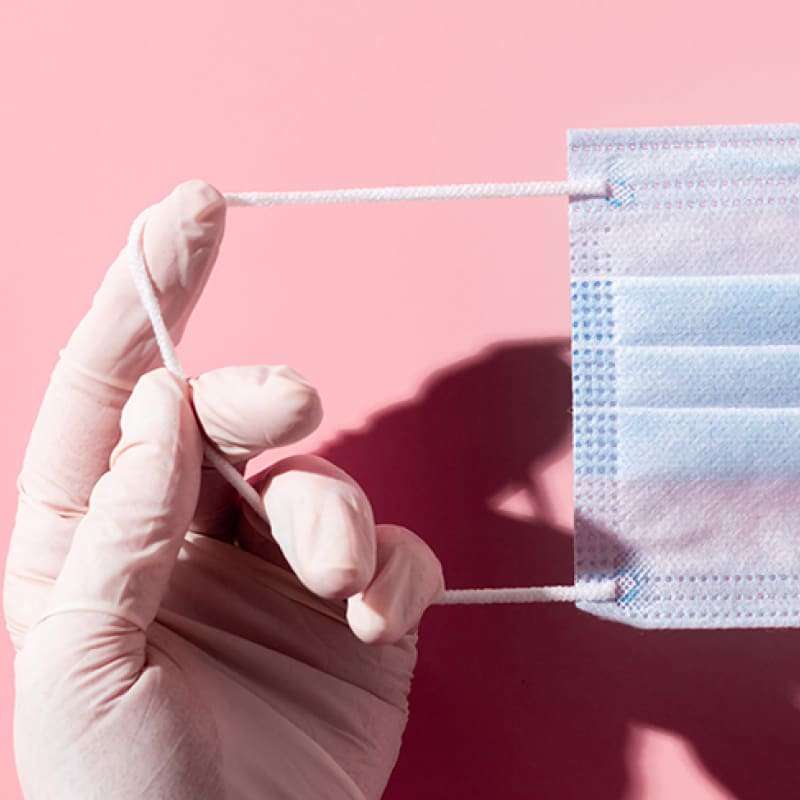 Hands holding blue surgical mask on pink background, lockdown update, e-Surgery