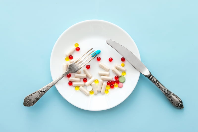 White plate on a blue background with a knife and fork . The plate contains a variety of pills in shape and colour. | Orlistat & Xenical:, Do weight loss pills work? | e-Surgery