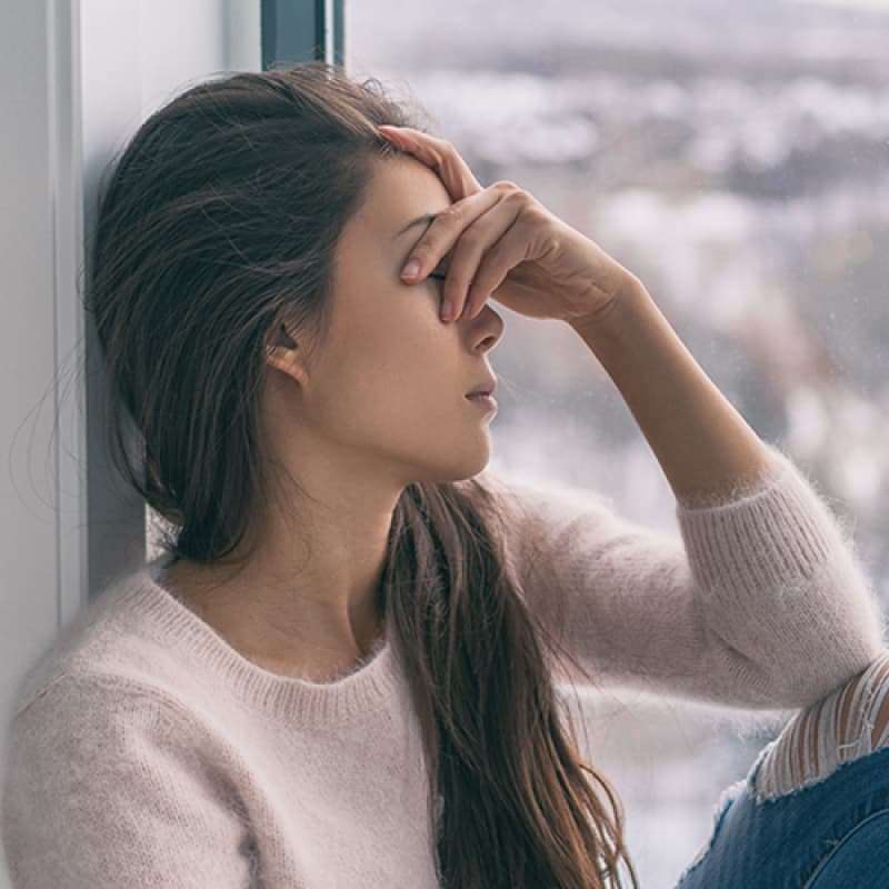 Seasonal Affective Disorder, woman sitting by a window with her head in her hands, e-Surgery