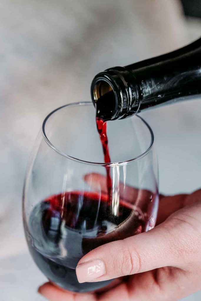 Close up of a woman's hands with painted fingernails pouring red wine from a bottle into a glass | Does Your Diet Trigger Migraines? | e-Surgery