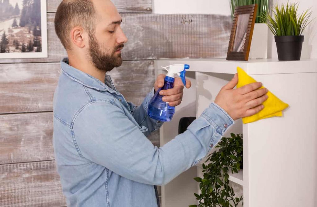Middle aged bald man with a beard, dusting a white counter with a yellow cloth | How To Deal With Winter Asthma | e-Surgery