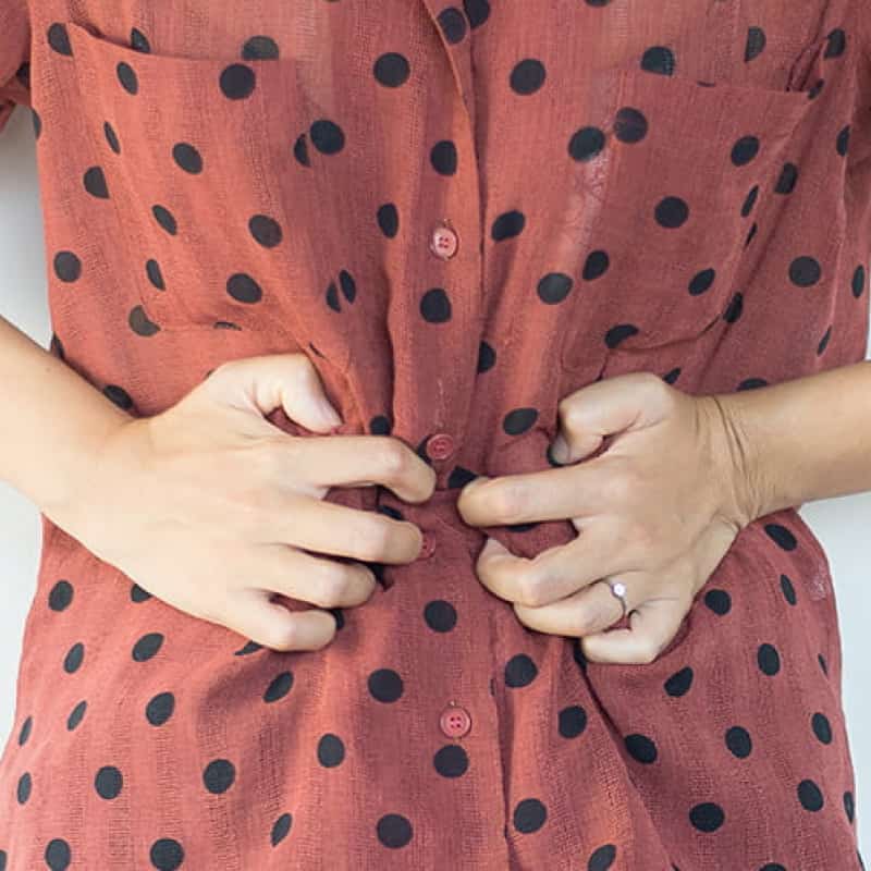 Woman in red, spotty shirt clutching stomach, home remedies for UTI, e-Surgery
