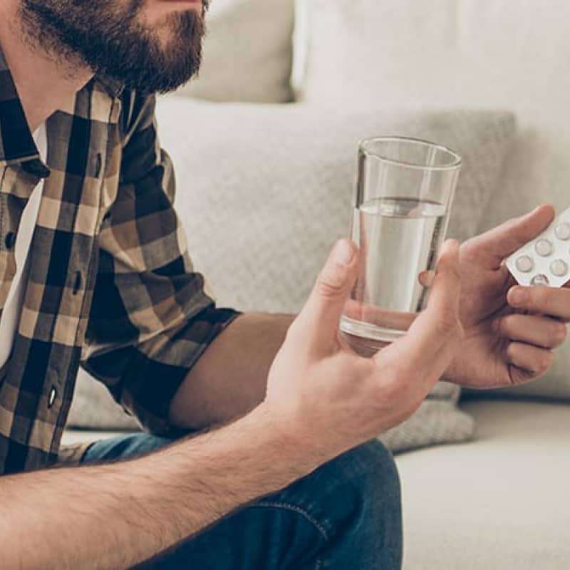 Man in checked shirt sitting on sofa comparing medication whilst looking at phone, kamagra is an unlicensed Erectile dysfunction medication, e-Surgery