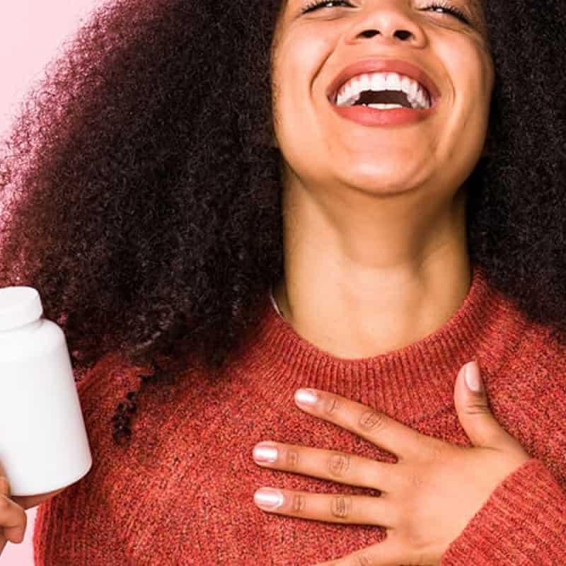 Woman smiling against pink background holding white pill pot, does lovegra work? e-Surgery