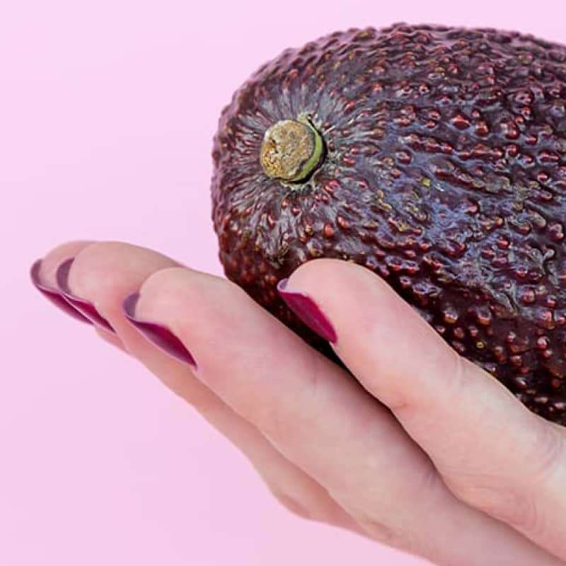 Hand holding avocado on pink background, naturally lower your cholesterol, e-surgery